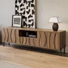 A modern wooden TV stand with decorative carvings and black metal legs, placed in a living room setting with artwork and a lamp. Anteprima dell’immagine prodotto