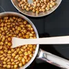 Nuts being cooked in a pan with a wooden spoon, with more nuts in a separate dish. Podgląd zdjęcia produktu