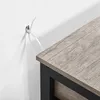 A close-up view of a cable tie attached to a wall, with the corner of a wooden table visible. Produktbild-Vorschau