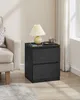A black wooden nightstand with two drawers sits next to a beige sofa and a white sheer curtain. Náhled obrázku produktu