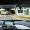 View from inside a car, showing the dashboard, rearview mirror with a driver's reflection, and a dashcam mounted on the windshield. Produktbild-Vorschau