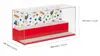 A clear display case with a red base and gray platforms, designed for displaying LEGO creations. The back wall features a colorful pattern of LEGO bricks and figures. Voir les images du produit
