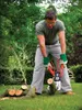 A man is using an electric chainsaw to cut logs in a garden. Produktbild-Vorschau
