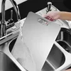 A person is rinsing a stainless steel cutting board under a faucet in a kitchen sink. Produktbild-Vorschau