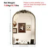 A decorative arched mirror with a floral motif at the top, displayed in a room setting with framed pictures and decorative objects on a shelf below. Podgląd zdjęcia produktu