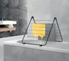 A black metal drying rack with a yellow towel is placed on top of a bathtub in a modern bathroom. Voir les images du produit