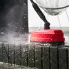 A red pressure washer head is cleaning dark, textured blocks, with water spraying. Voir les images du produit
