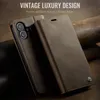 A brown leather flip phone case is shown, with the phone partially inserted. The case is closed and lying on a textured brown surface. Produktbild-Vorschau