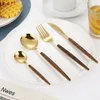 A set of golden cutlery with wooden handles is arranged on a white plate, with waffles and a drink in the background. Produktbild-Vorschau