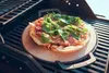 A pizza is being grilled on a pizza stone on a barbecue grill. Podgląd zdjęcia produktu
