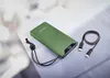 A green power bank with a black charging cable and lanyard on a light gray and white surface. Voir les images du produit