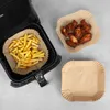 An overhead shot of an air fryer basket filled with french fries, and two paper liners, one with chicken wings and one empty. Podgląd zdjęcia produktu