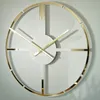 A modern wall clock with a gold frame and white face, mounted on a light gray wall. Náhled obrázku produktu