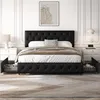 A bedroom scene featuring a tufted black bed with integrated pet beds. The room is decorated in a modern, elegant style with white paneled walls and a framed abstract artwork above the headboard. Produktbild-Vorschau