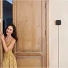 A woman is opening a wooden door, and a smart home device is mounted on the wall next to the door. Anteprima dell’immagine prodotto