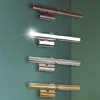 Four wall-mounted lights in different finishes are displayed on a teal-green wall. Podgląd zdjęcia produktu