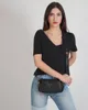 A woman wearing a black top and blue jeans poses with a black crossbody bag. Produktbild-Vorschau