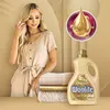 A woman is standing next to a stack of towels and a bottle of Woolite laundry detergent. The background is a warm, neutral tone. Podgląd zdjęcia produktu