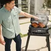 A man is grilling two chickens on a black electric grill on a patio. Voir les images du produit