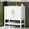 A white bathroom vanity with a gold faucet and brass handles is shown in a bathroom setting with green walls and a patterned floor. Náhľad obrázku produktu