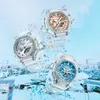 Three transparent G-Shock watches with different colored faces (silver, rose gold, and blue) are shown floating in a stylized environment with shattered glass-like elements and water. Produktbild-Vorschau