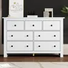 A white dresser with black knobs is shown in a room with a black textured wall and a rug on the floor. Produktbild-Vorschau