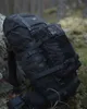 A black backpack is leaning against a rock in a forest setting. Produktbild-Vorschau