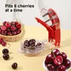 A cherry pitter tool is shown with cherries in a basket and in a bowl. Náhled obrázku produktu