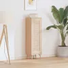 A tall, narrow wooden cabinet with louvered doors is placed next to a floor lamp and a large potted plant. The image is taken indoors with a neutral white background and a wooden floor. Náhled obrázku produktu
