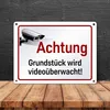 A metal sign indicating video surveillance is displayed on a wooden surface against a dark textured background. Produktbild-Vorschau