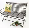 A metal garden bench with a decorative pillow and a small potted plant. Produktbild-Vorschau