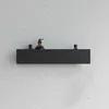 A black shelf mounted on a textured gray wall, with two dark glass bottles on it. Produktbild-Vorschau