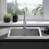A kitchen sink and faucet are shown in a well-lit kitchen setting, with plants on the windowsill and a view of greenery outside. Podgląd zdjęcia produktu