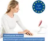 A woman is sitting at a table with an infrared lamp in front of her. Produktbild-Vorschau