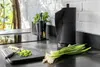 A kitchen counter with chopped green onions on a cutting board, a bunch of green onions, and a black paper towel holder. Anteprima dell’immagine prodotto