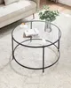 A round glass coffee table with a black metal frame on a light-colored rug, next to a couch. Náhled obrázku produktu