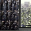 A close-up of a dark floral patterned curtain hanging next to a window with a city and forest view. Produktbild-Vorschau