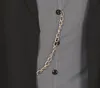 A close-up view of a black jacket with a gray inner lining, featuring a decorative gold chain and black buttons. Produktbild-Vorschau