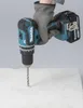 A gloved hand holding a cordless drill, drilling into a light-colored surface. Produktbild-Vorschau