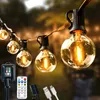A string of illuminated globe-shaped LED lights hangs outdoors, with a solar panel, remote control, and USB cables visible in the foreground. Produktbild-Vorschau