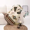 A boho-style blanket draped over a white sofa, with a hat and decorative items on a round rug in the foreground. Produktbild-Vorschau