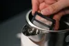 A hand is holding a filter over the opening of a white and stainless steel electric kettle. Voir les images du produit