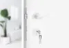 A close-up shot of a white door handle and lock mechanism with keys inserted. Produktbild-Vorschau
