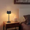 A black LED bedside lamp is placed on a wooden nightstand next to a tissue box and a bed. Produktbild-Vorschau