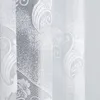 A close-up view of a white lace curtain with a floral pattern. Produktbild-Vorschau