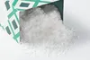 A box of Maldon Sea Salt Flakes is tipped over, spilling the salt onto a white surface. Podgląd zdjęcia produktu