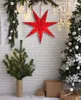 A festive Christmas scene with a red star decoration, a small Christmas tree, and a larger decorated Christmas tree. Podgląd zdjęcia produktu