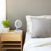 A white portable fan sits on a wooden nightstand next to a potted plant and a bed. Produktbild-Vorschau