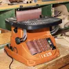 A woodworking tool, specifically a spindle sander, is shown on a workbench in a workshop setting. Podgląd zdjęcia produktu