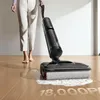 A person is using a black electric mop on a wooden floor, cleaning up a spill. Produktbild-Vorschau